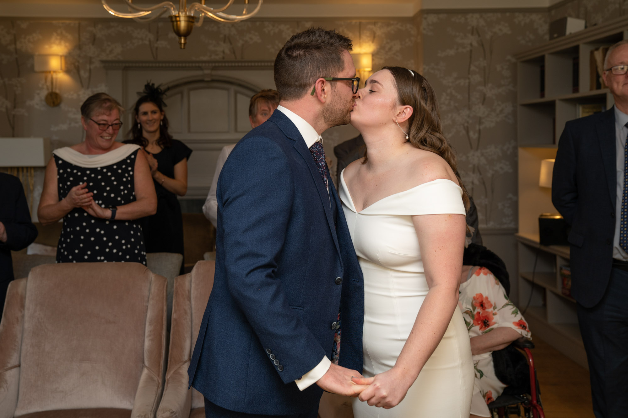 Bride and groom sharing their first kiss as husband and wife in the ceremony room at Crag Wood, guests clapping behind them