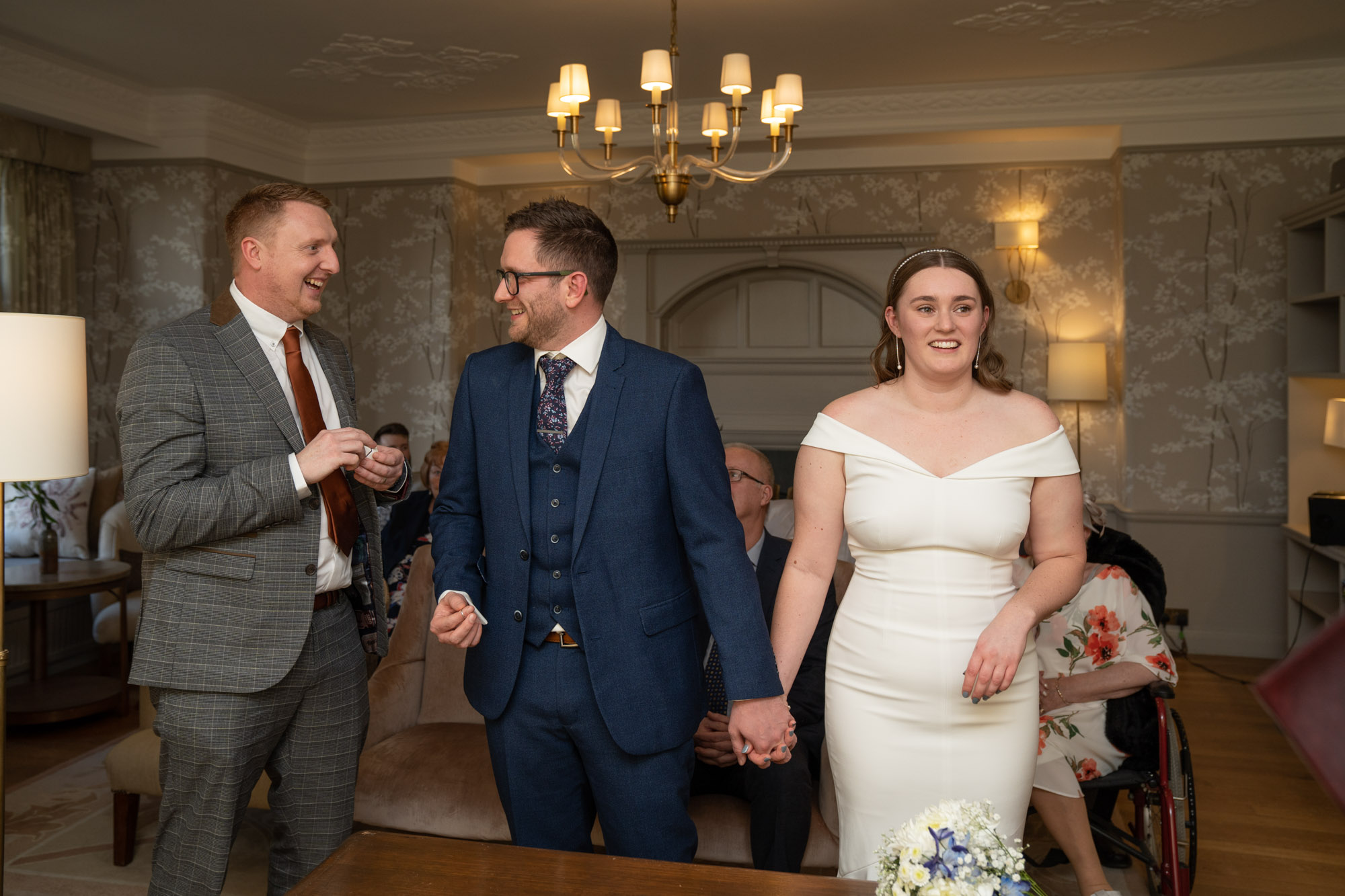 Best man handing the wedding ring to the groom inside the ceremony room at Crag Wood, bride smiling beside him, guests standing around