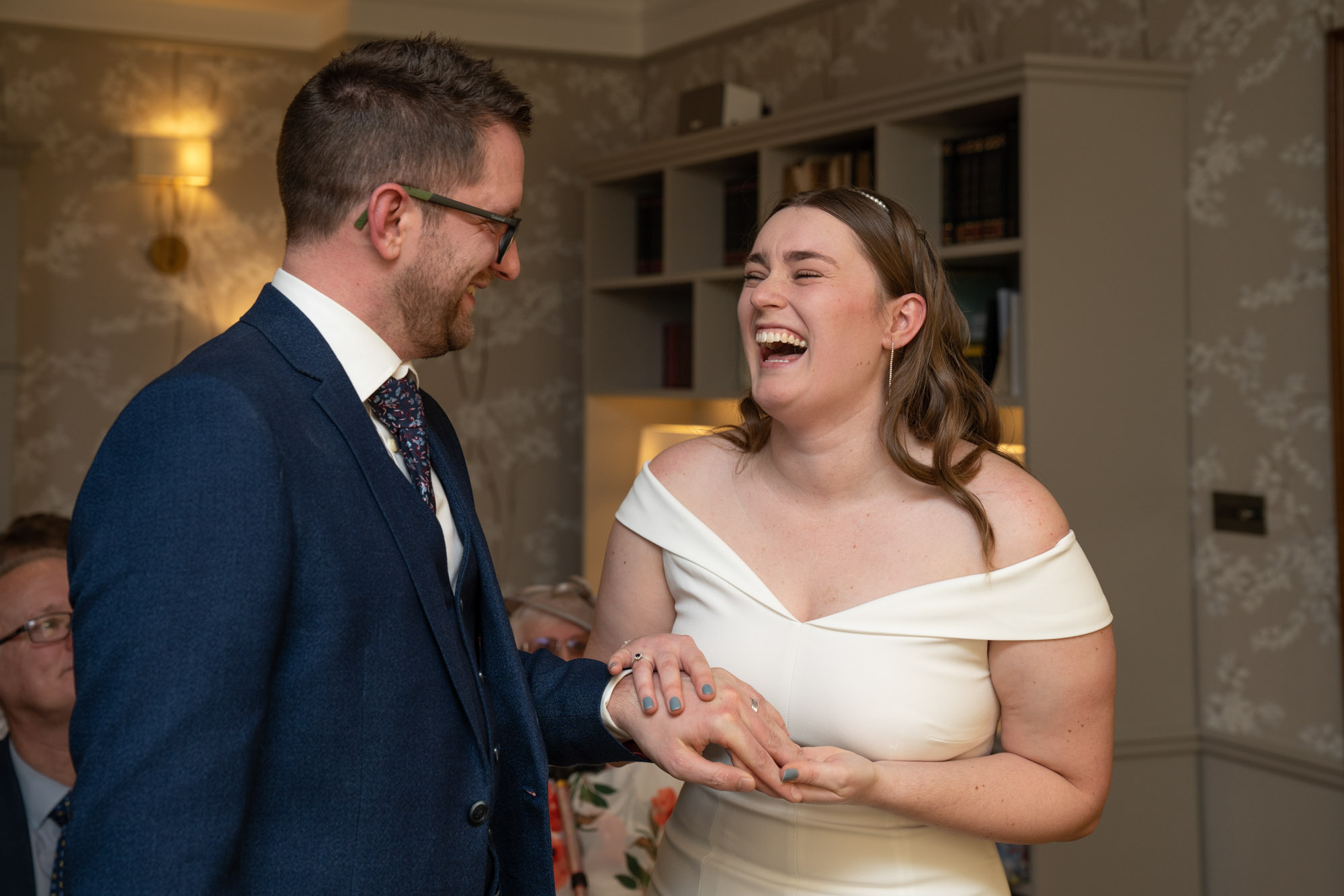 Bride laughing openly as the groom looks at her hand during the ring exchange inside the ceremony room at Crag Wood