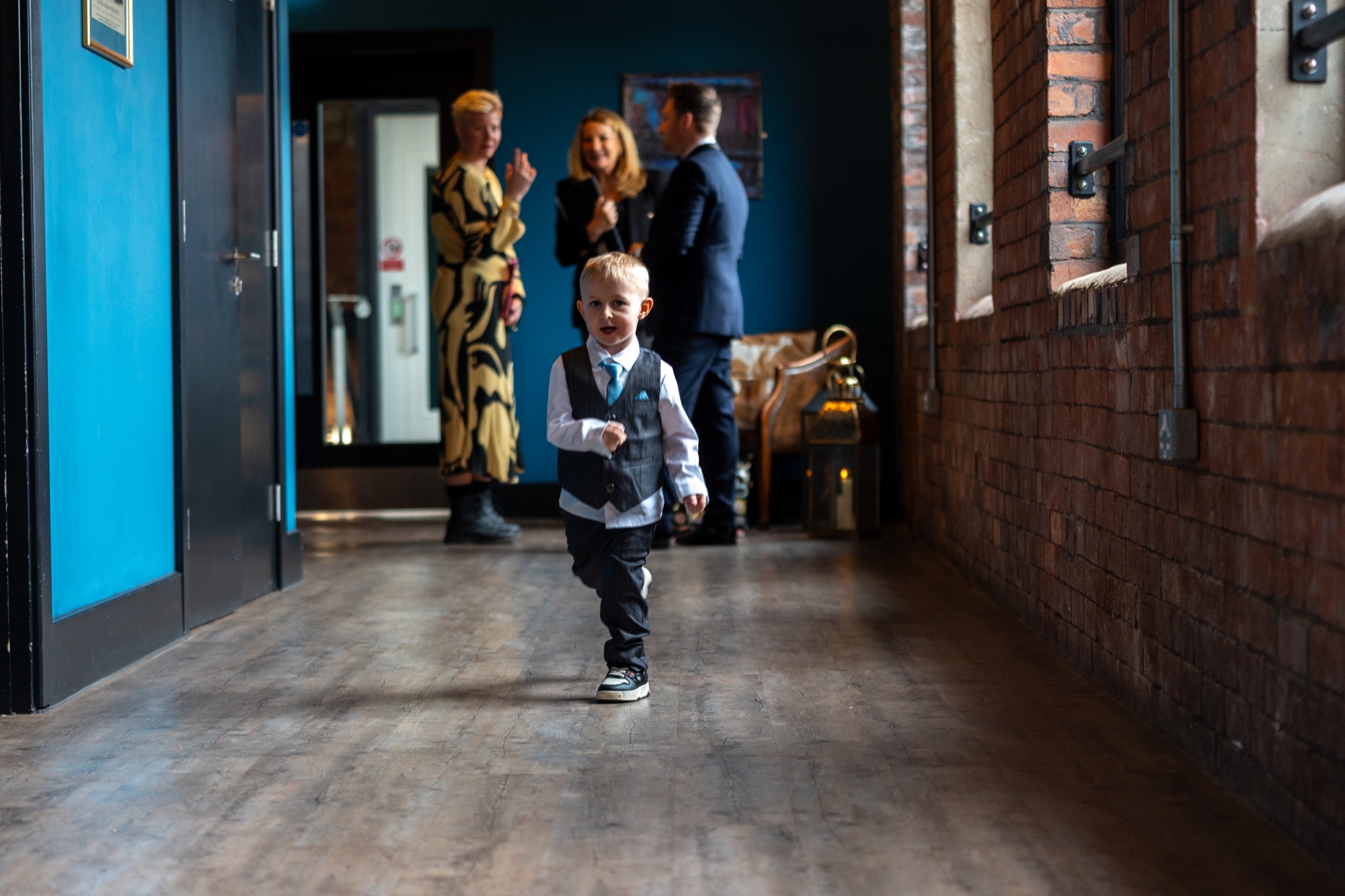 A small pageboy in a waistcoat walking alone down a blue-painted corridor