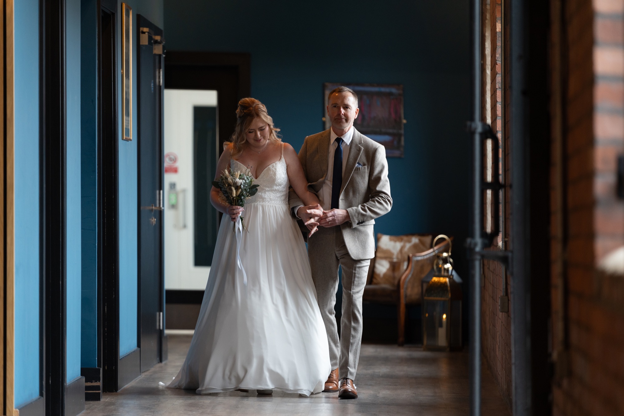 The bride's father walking her down a corridor towards the ceremony, her arm linked through his