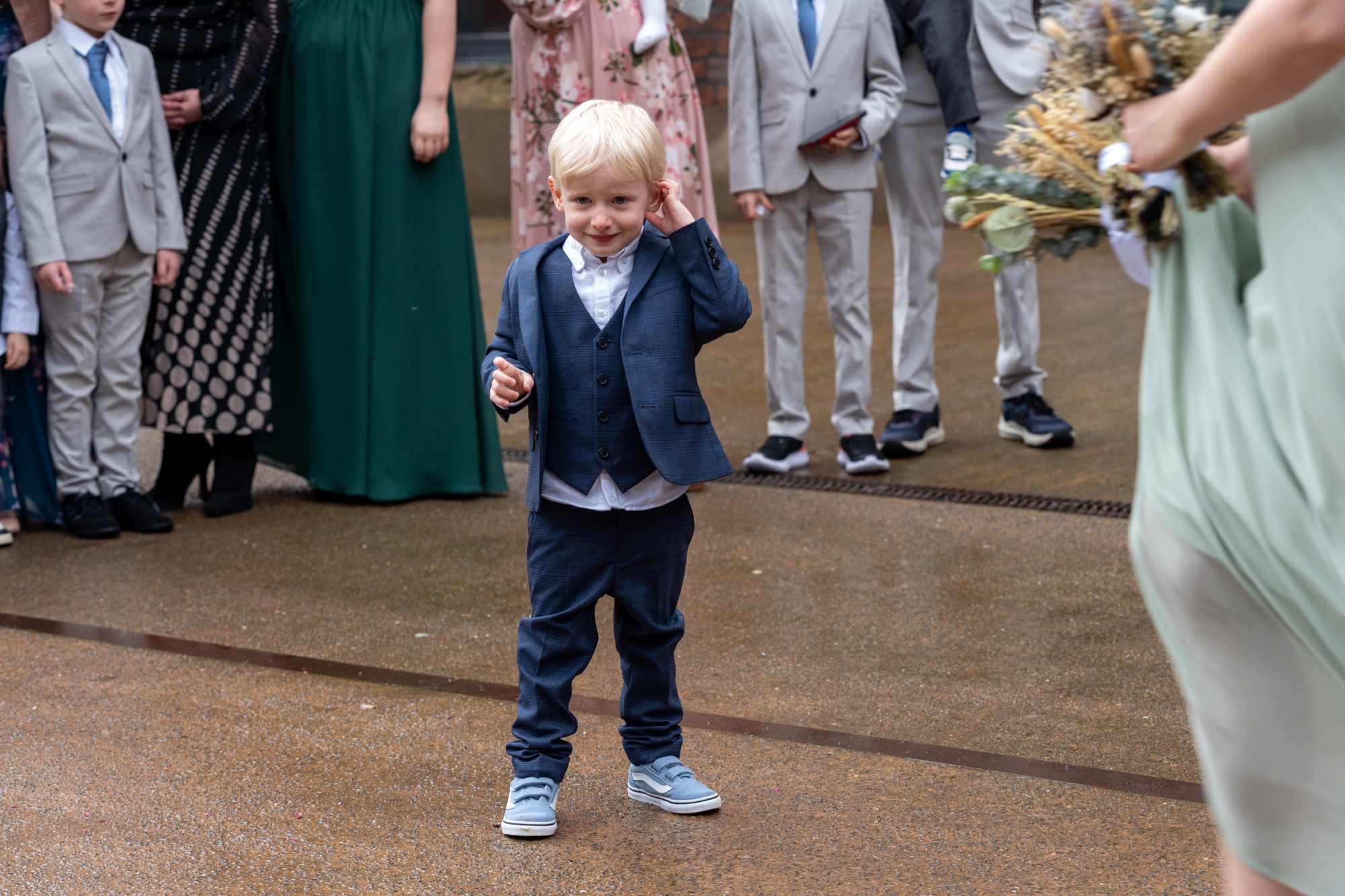 A young pageboy in a navy waistcoat pulling a funny face outside after the ceremony