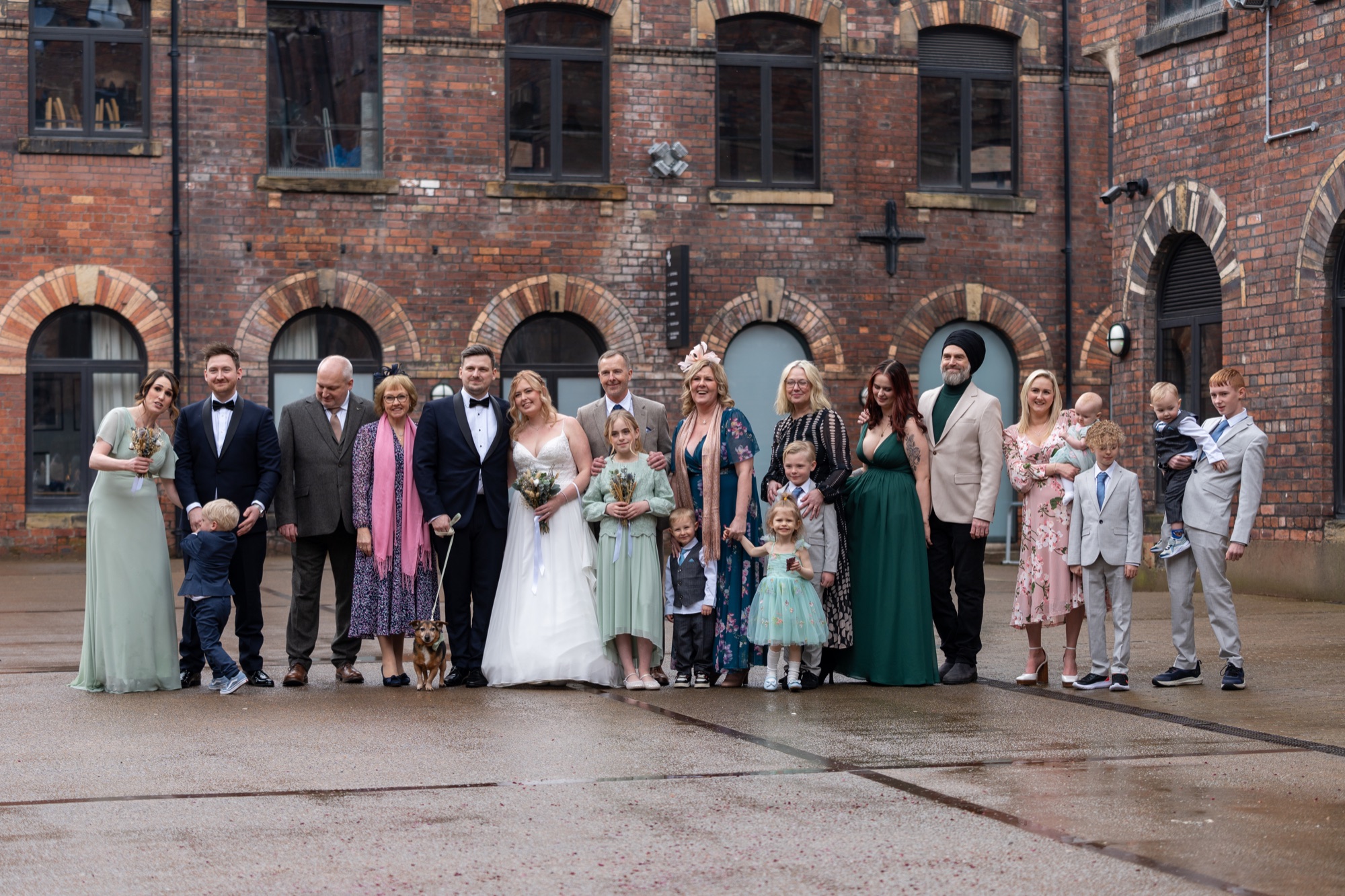 The wedding party and family posing together outside a red-brick building