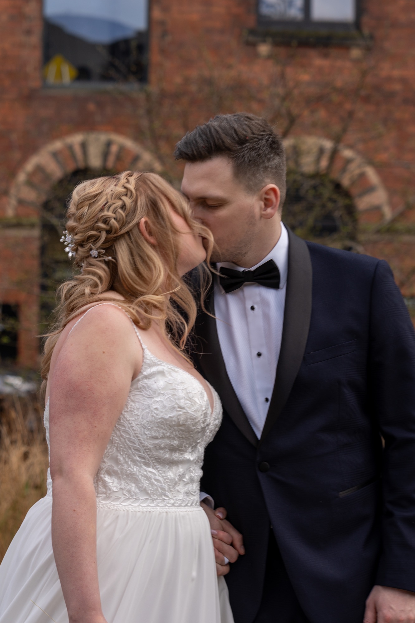 A close-up portrait of the bride and groom kissing in front of a red-brick wall