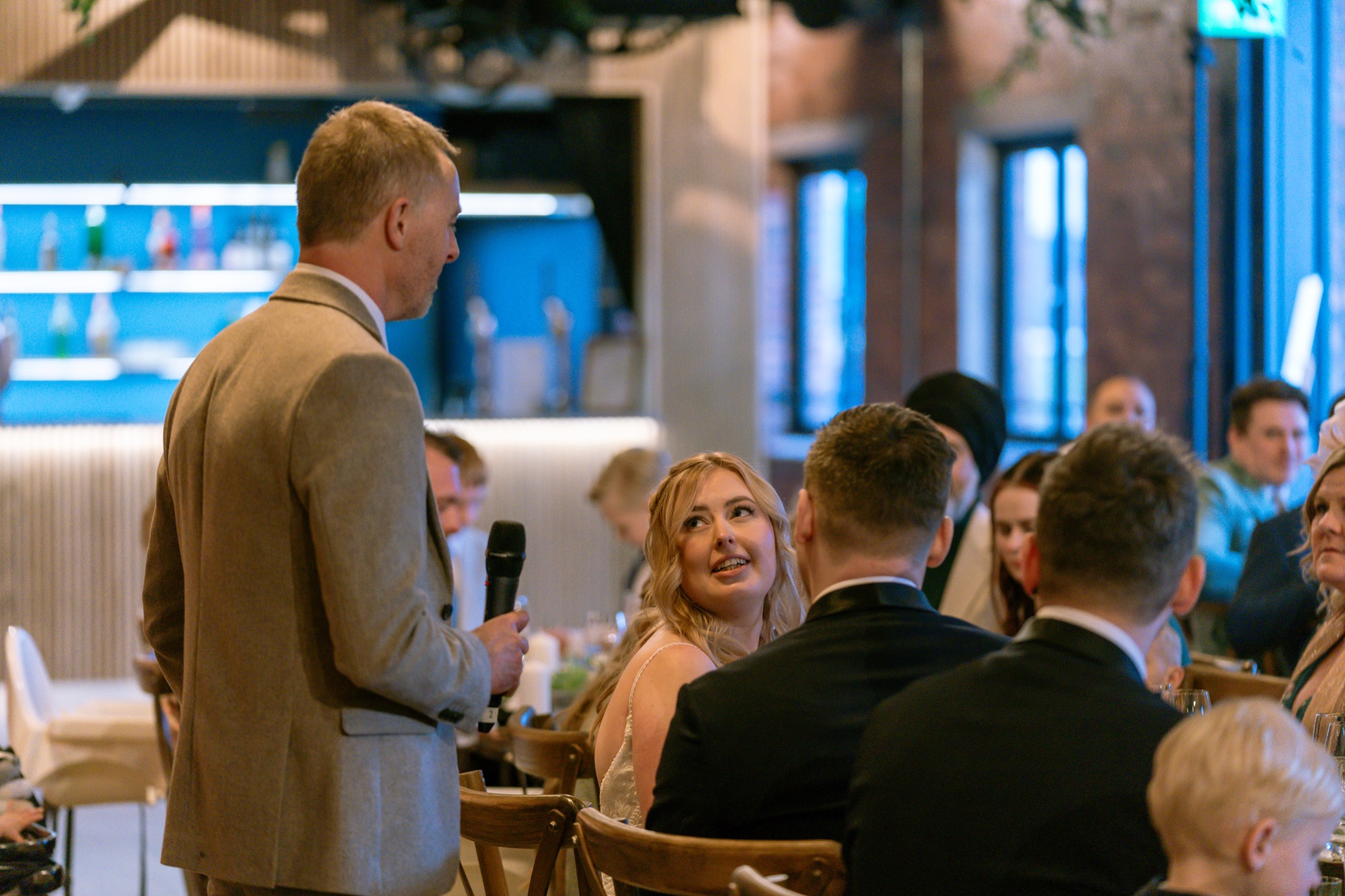 The best man giving his speech as the bride and groom listen at the top table, fairy lights behind