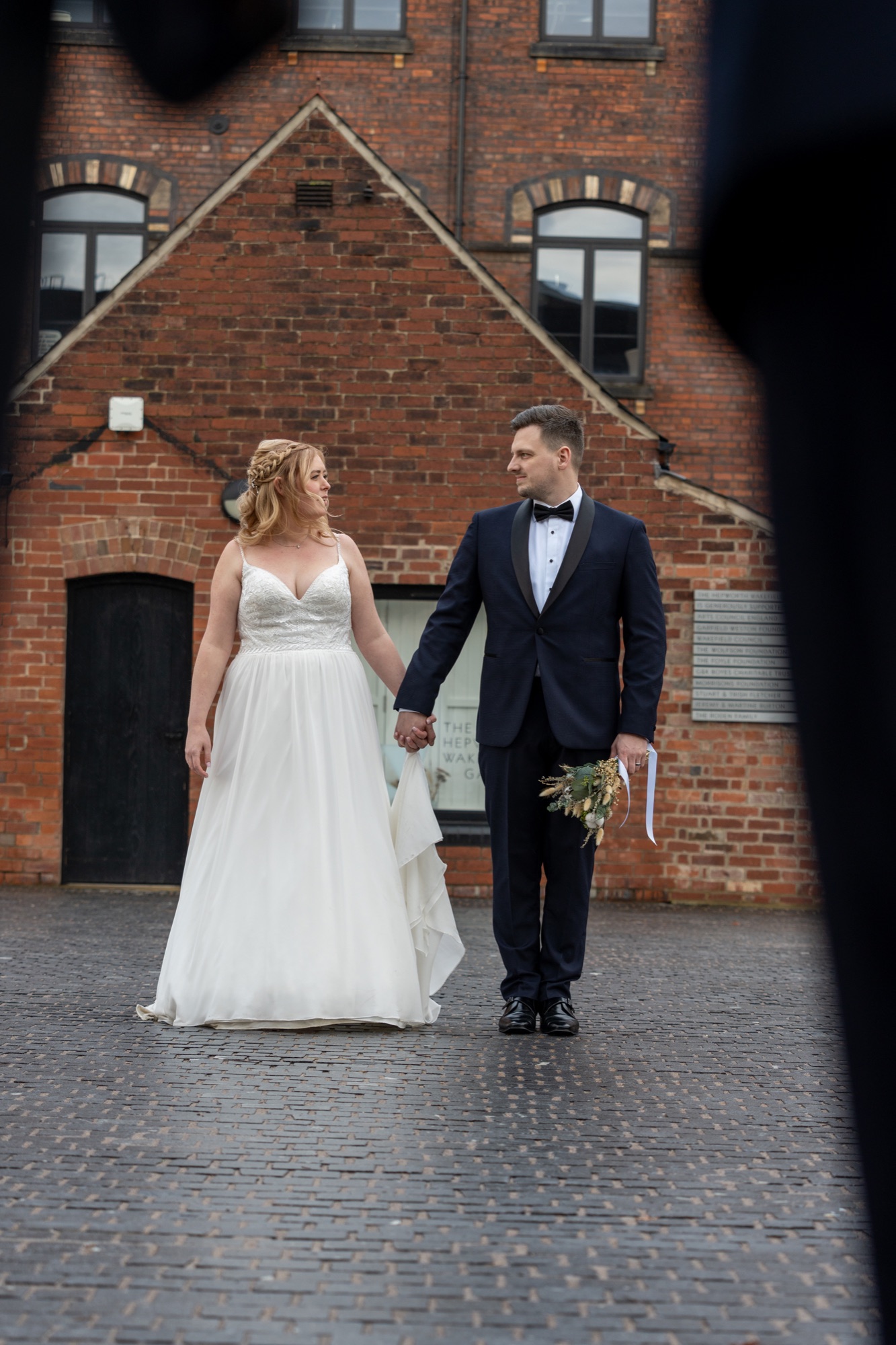 A full-length portrait of the bride and groom walking together across a cobbled courtyard
