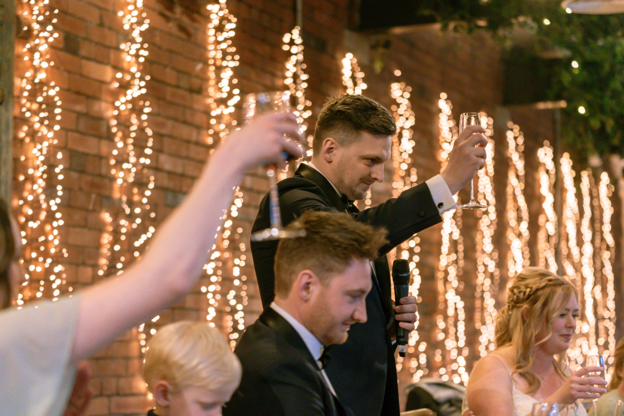 Guests raising their glasses in a toast to the newlyweds under strings of fairy lights