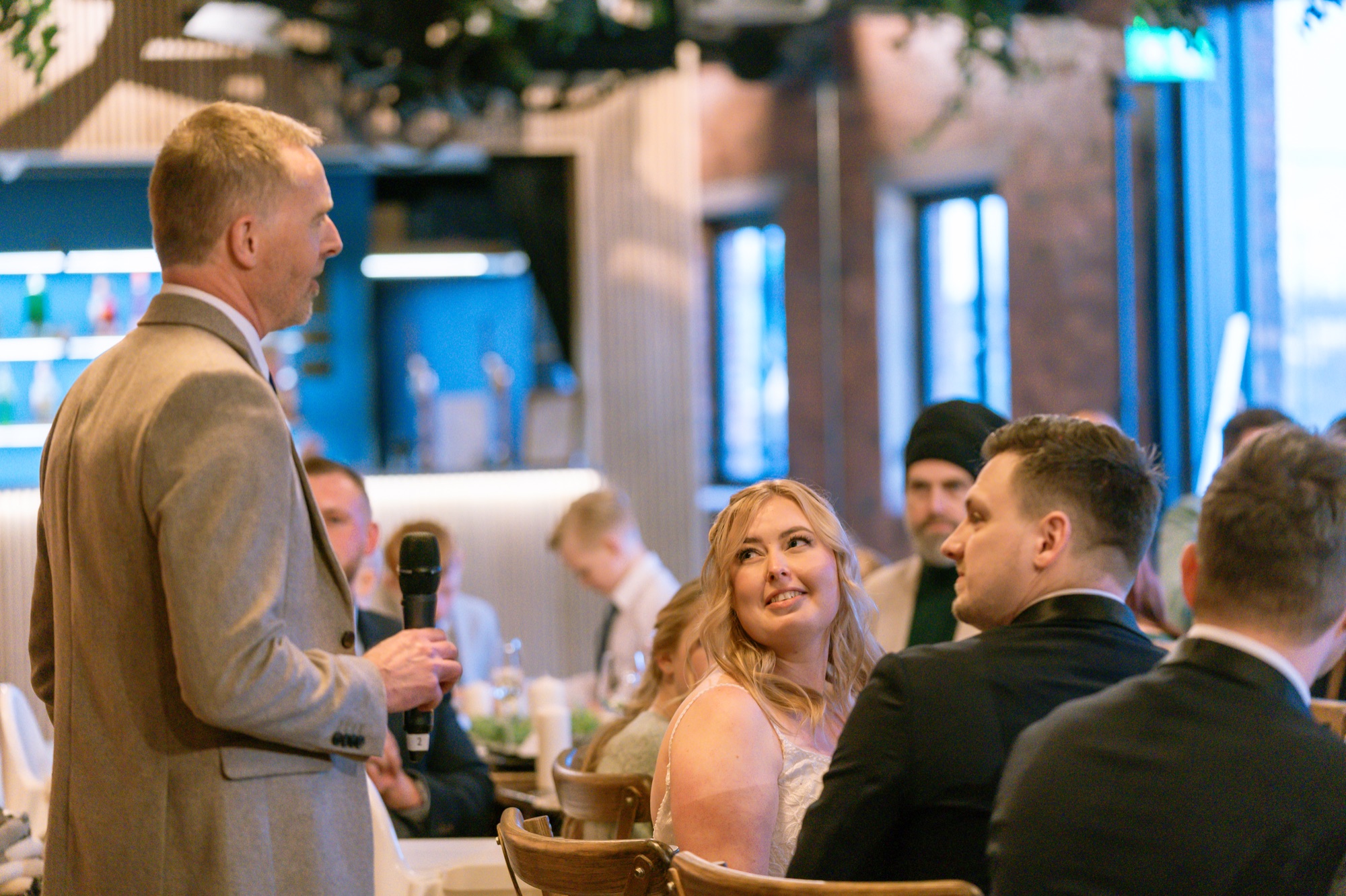 The groom laughing during a wedding speech, the bride smiling beside him