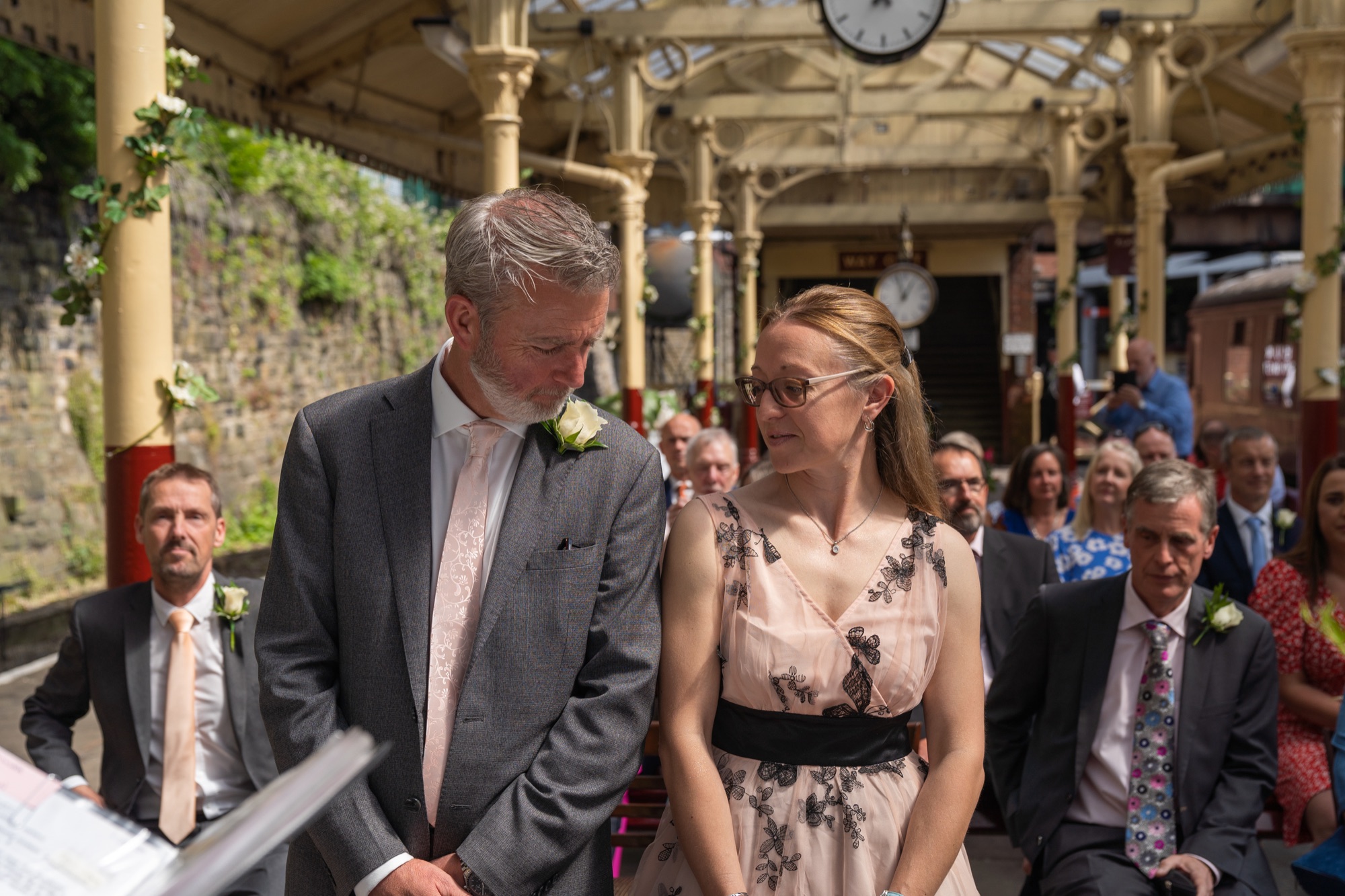 Bride laughing mid-ceremony on the station platform, guests seated behind her under the canopy