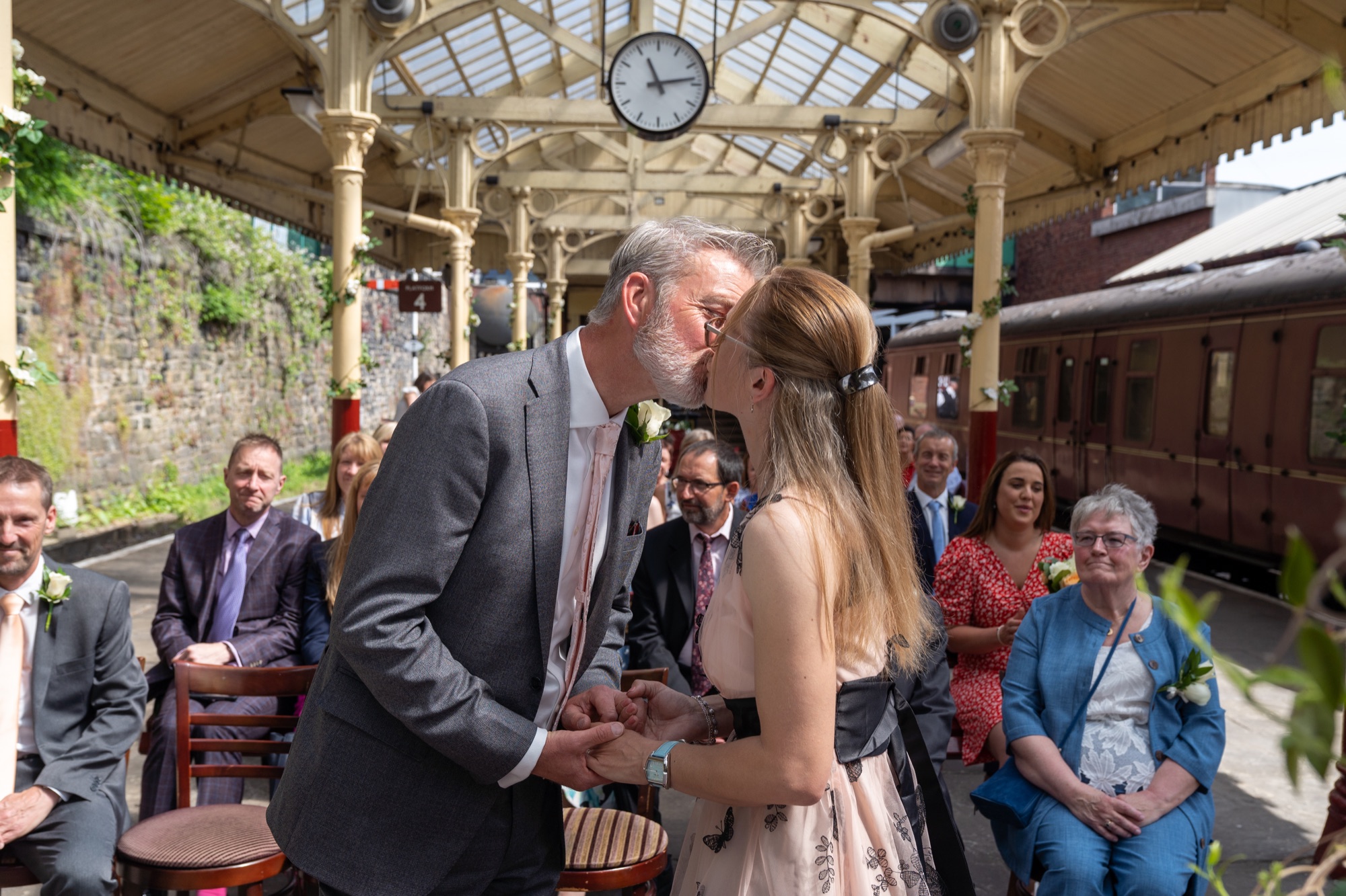 Groom resting his forehead against the bride's during the vows, station clock visible above them