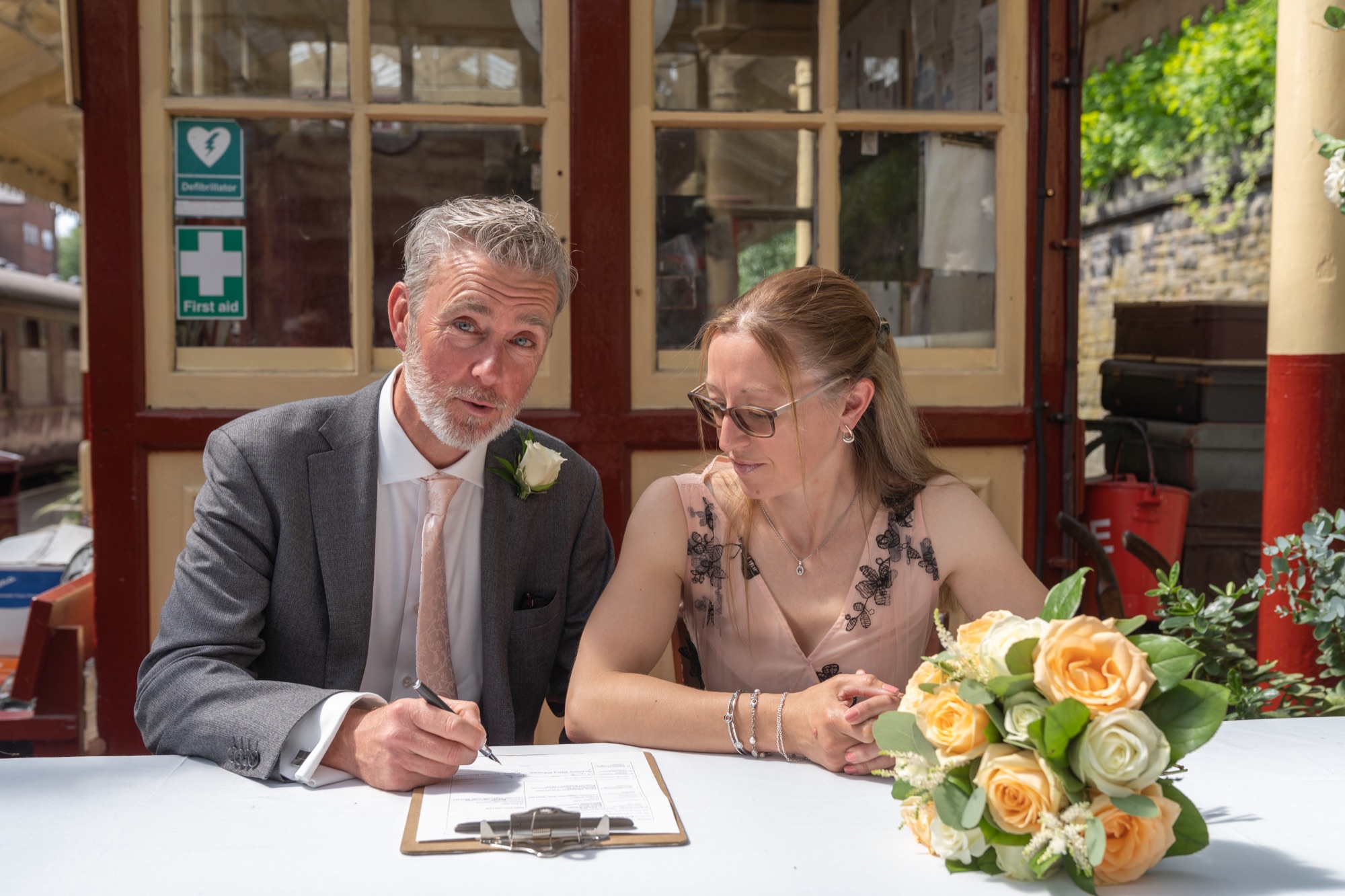 Bride and groom signing the register at a table on the platform with a witness looking on
