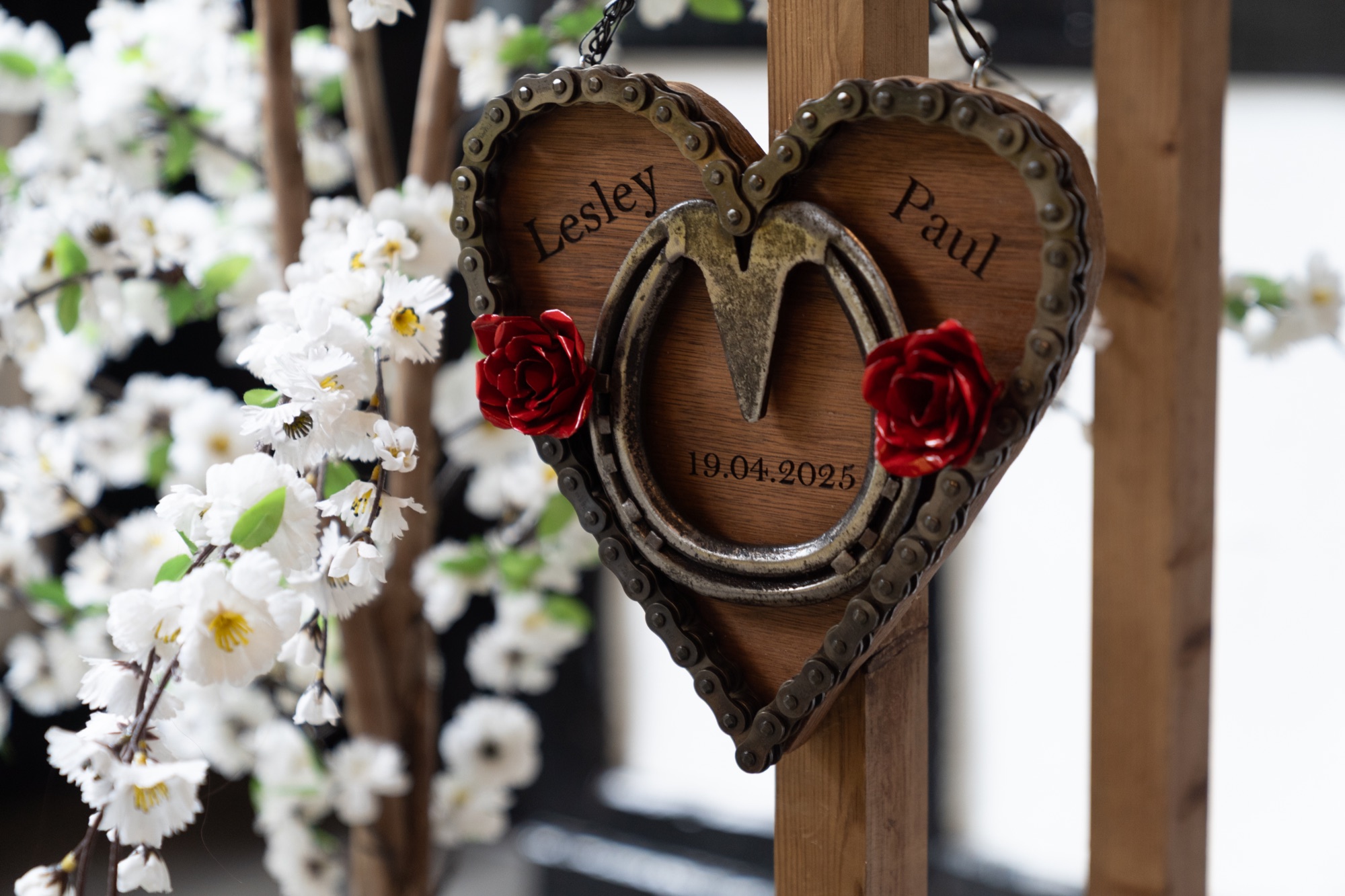 A personalised wooden heart decoration with the couple's names and wedding date, hung among blossom at the ceremony entrance.