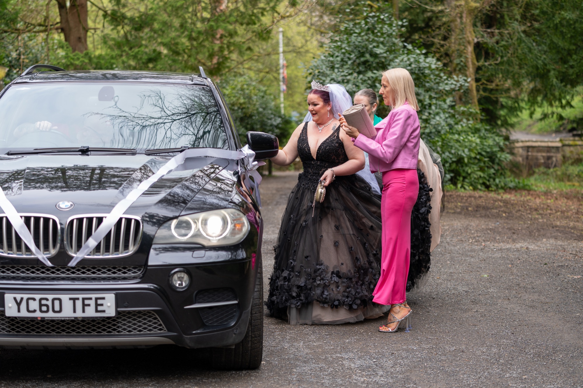 The bride arrives at Olde England Kiosk in a ribbon-decorated car, helped from the vehicle by family.