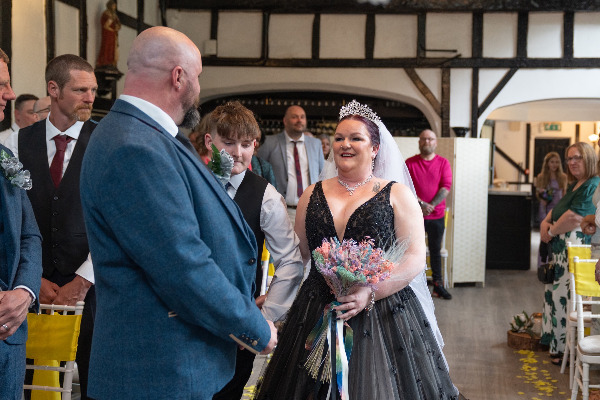 The bride walks down the aisle inside the timber-framed ceremony room as the groom watches on.