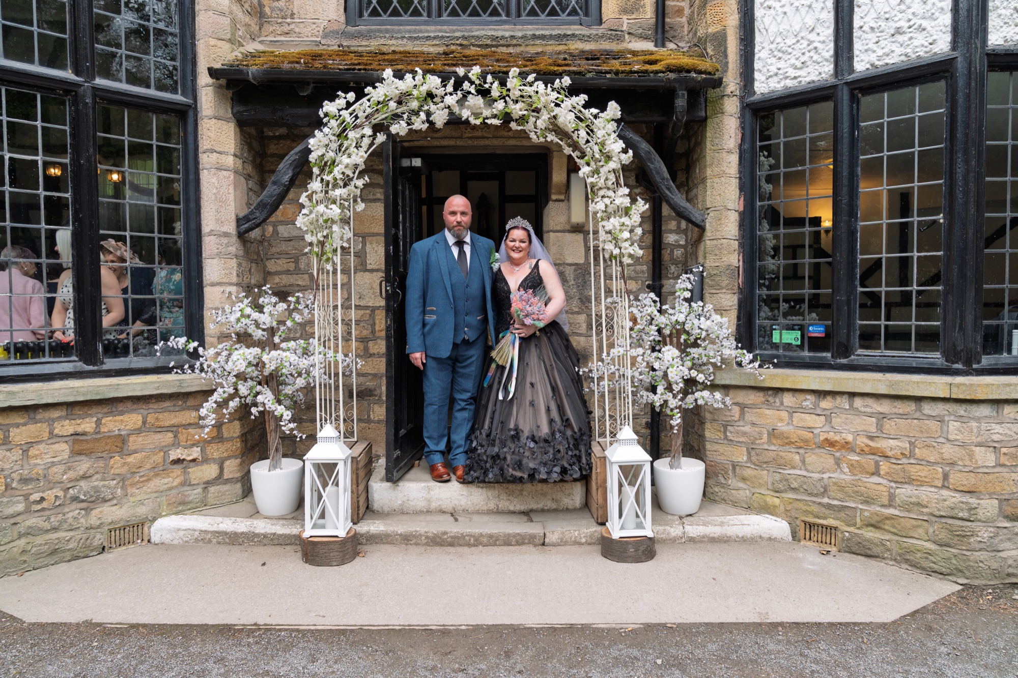 The bride and groom pose under the blossom-covered archway at the entrance to Olde England Kiosk.