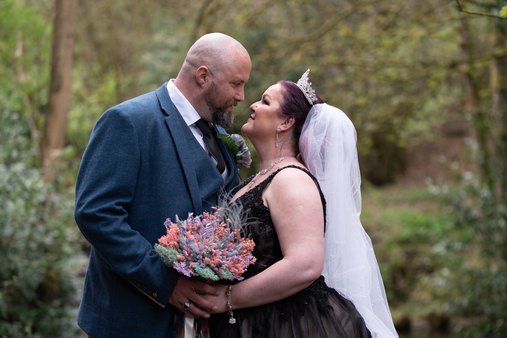 A close couple portrait in the woodland, foreheads together, surrounded by trees.