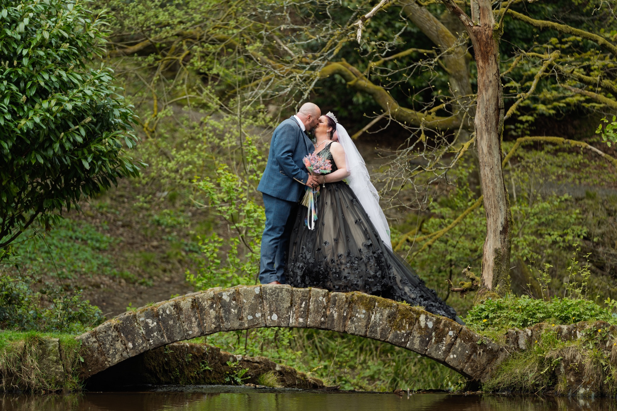 The newlyweds kiss on the stone bridge, the bride's black gown trailing across the stonework.