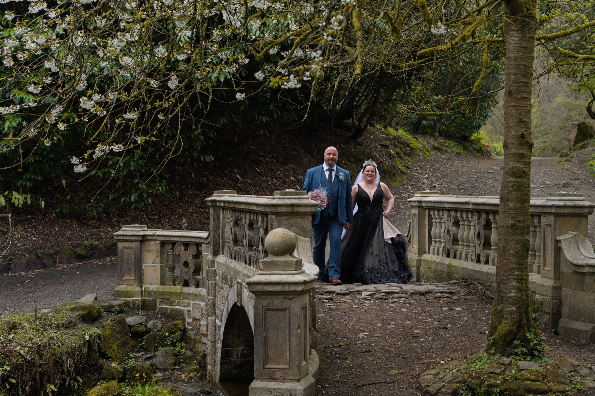 The couple pose on a stone balustrade beneath a blossoming tree in the wood.