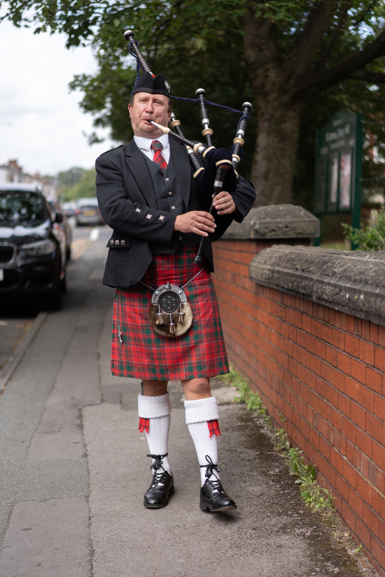 Piper in full Scottish dress playing bagpipes on the street before the ceremony