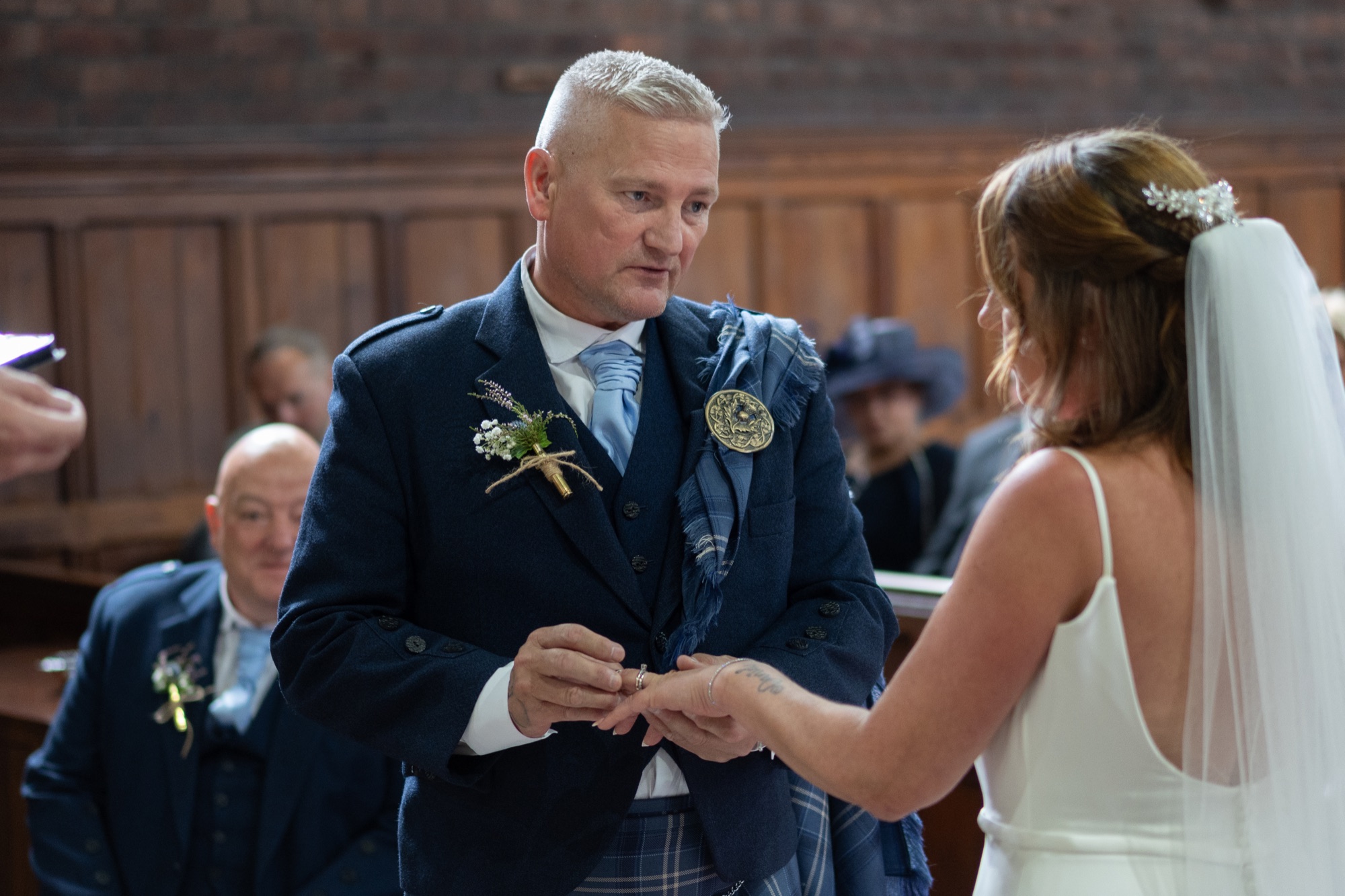 Groom in a kilt placing the ring on the bride's finger at the altar