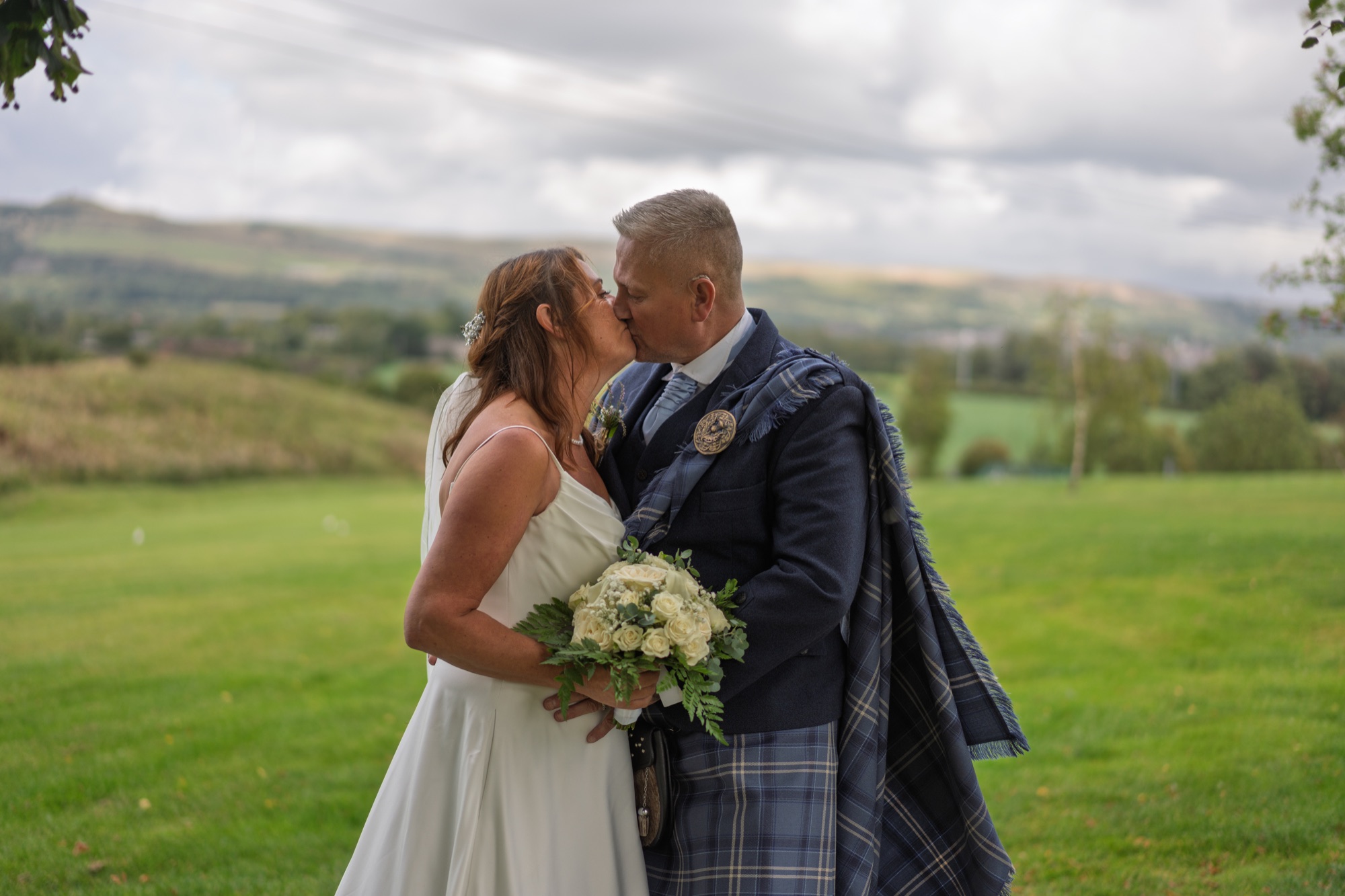 Bride and groom kissing with the Lancashire countryside behind them