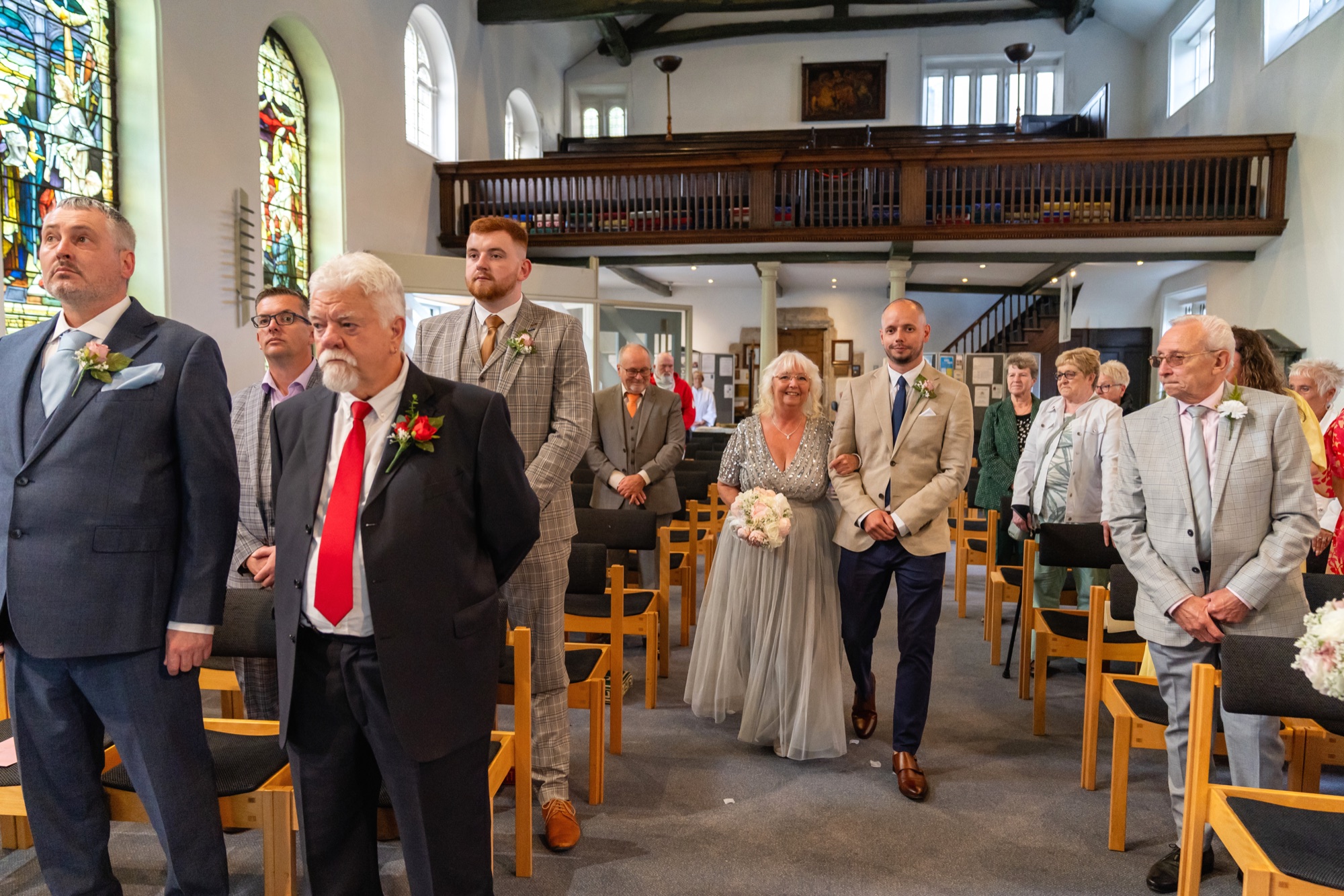 The bride walking up the aisle on a family member's arm, with the congregation watching