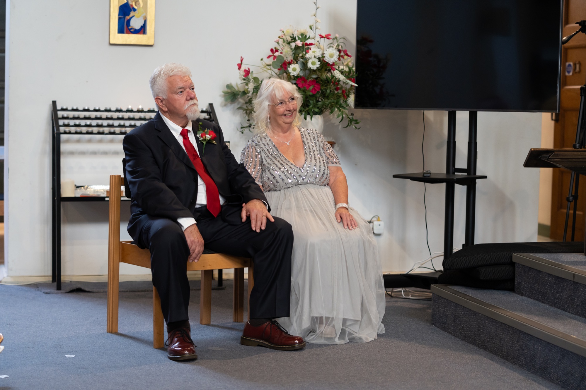 The newlyweds sitting together after the ceremony with flowers behind them