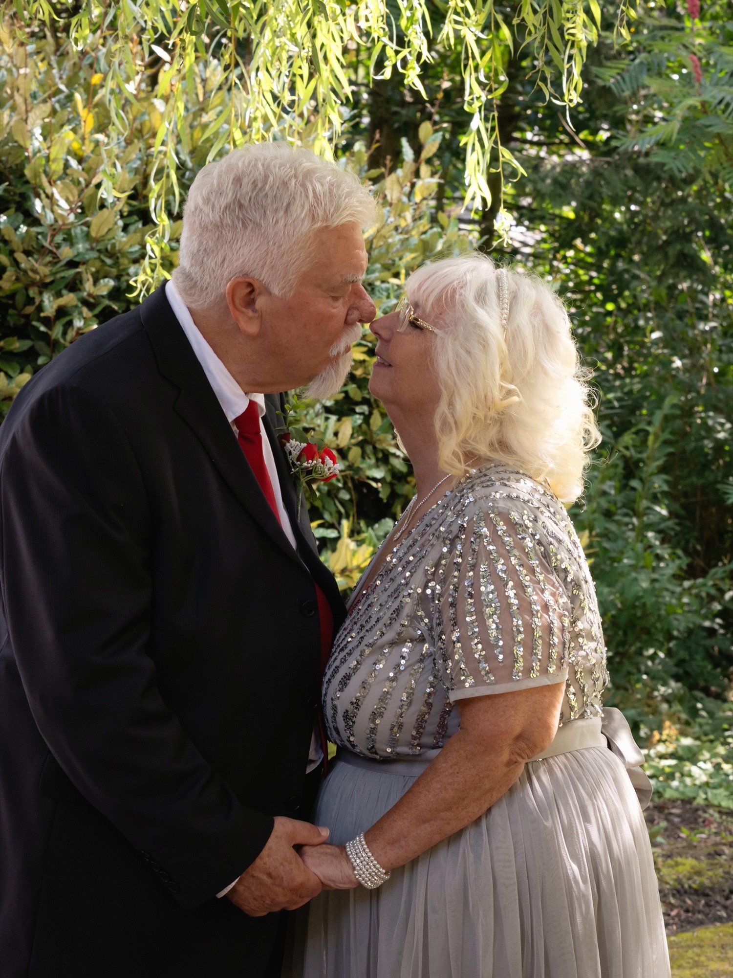The bride and groom share a kiss together in a garden during their portrait session
