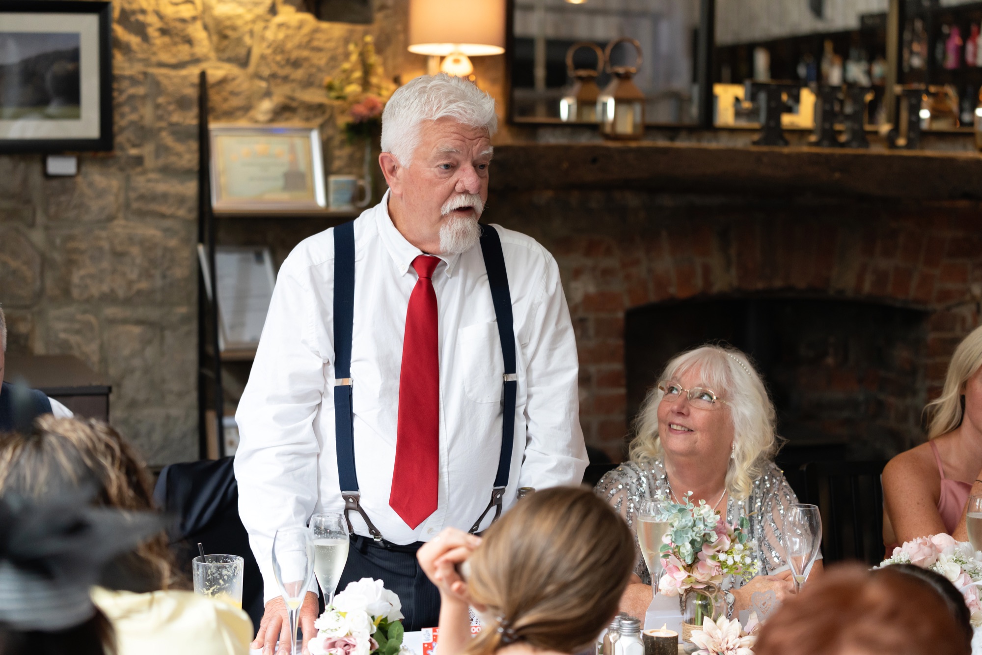 The groom giving his speech at the wedding meal, with the bride looking up at him